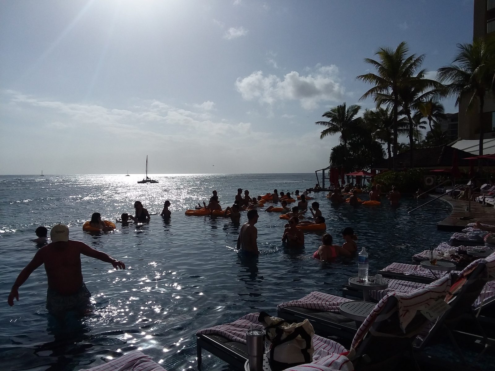 Swimmers in the Sheraton Waikiki infinity pool with a catamaran offshore