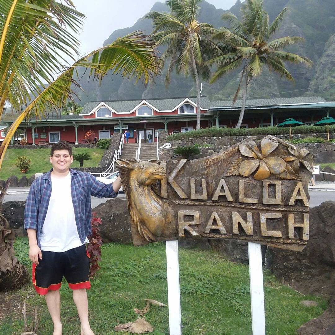 The carved Kualoa Ranch sign with the visitor center behind it