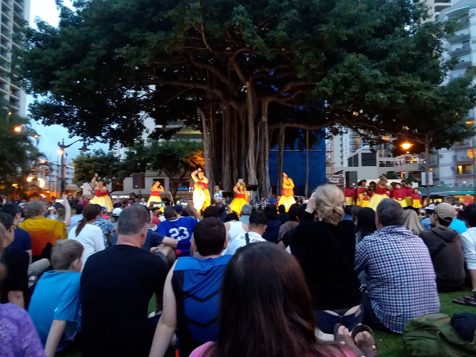 The free hula show at the Kuhio Beach Hula Mound at dusk — dancers under the banyan and the audience on the grass, March 2018