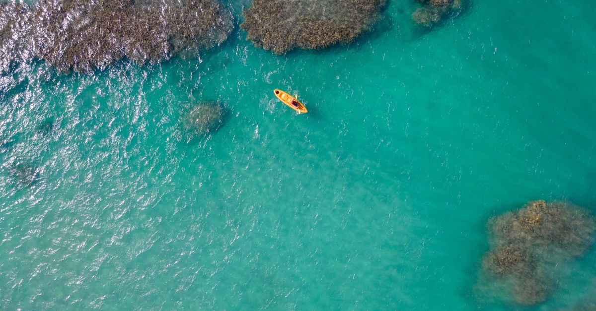 Aerial view of a yellow kayak on turquoise water over coral heads