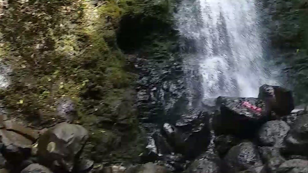 The base of Lulumahu Falls pouring onto boulders, a pink trail marker painted on one rock