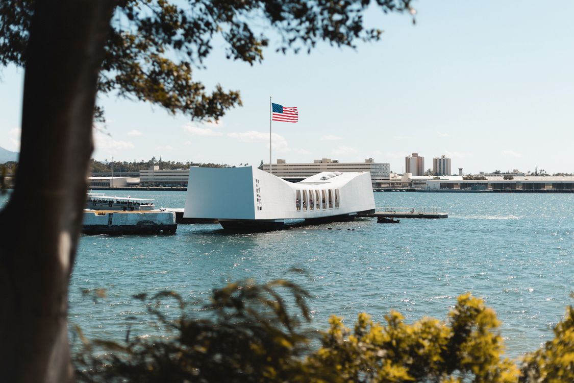 USS Arizona Memorial on the water with a tour boat alongside and the American flag flying
