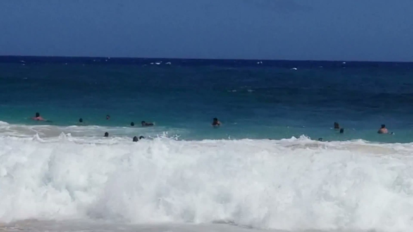 A wave crashing onto the sand at Sandy Beach while bodyboarders wait behind it