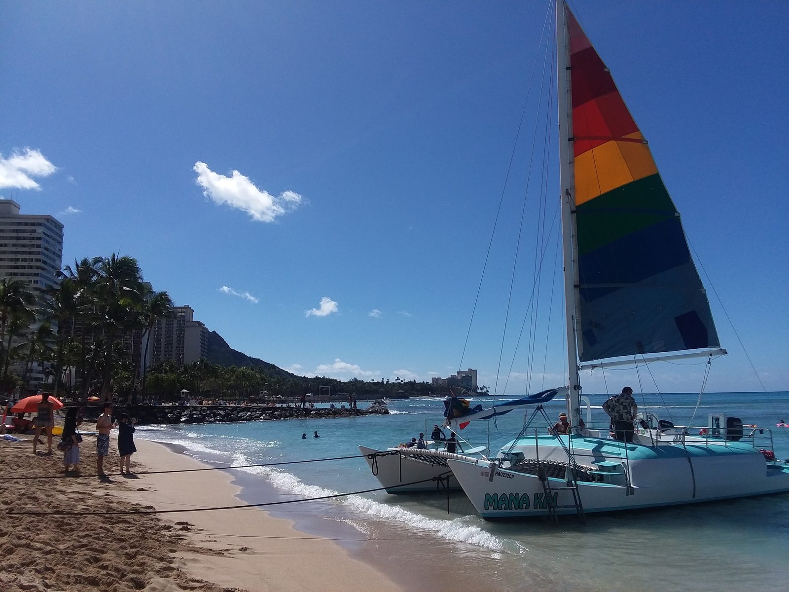 A catamaran boarding passengers off the sand at Waikiki Beach