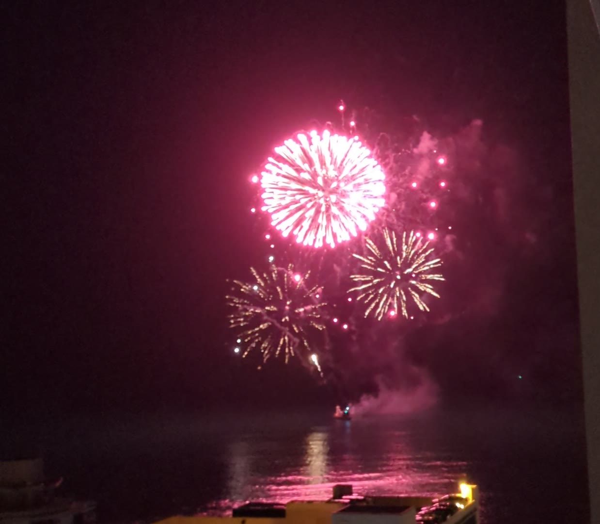 Fireworks bursting pink and gold over the water off Waikiki, seen from a lanai